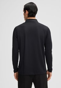 Polo a maniche lunghe nera con colletto, realizzata in tessuto morbido e caratterizzata da un design minimalista con un logo discreto sull'orlo.