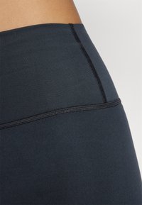 Leggings noirs taille haute avec une texture lisse, présentant une ligne de couture contrastante et un design sans coutures au niveau de la taille.