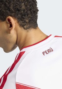 Wit sportshirt met rode accenten en strepen. "PERÚ" geborduurd op de bovenrug. Lichtgewicht, ademend materiaal. Gestructureerde stof.