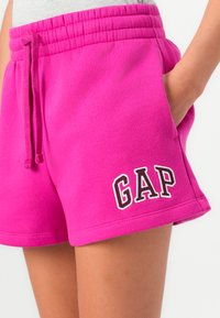 Rosa bomullsbyxor med resårmidja, med sidofickor och en vit "GAP"-logotyp på vänstra fållen. Slät textur, avslappnad passform.