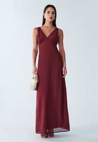 Burgundinmattinen maksimekko, jossa on V-pääntie, rypytetty yläosa ja valuva kangas. Yhdistettynä kultakuvioiseen clutch-laukkuun ja metallisiin korkokenkiin.