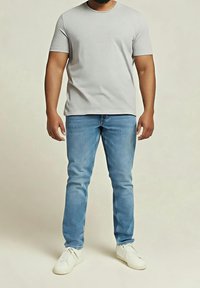 Szary t-shirt z krótkim rękawem, zestawiony z jasnoniebieskimi dżinsami i białymi sneakersami, z klasycznym okrągłym dekoltem i luźnym krojem.