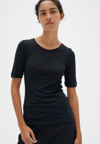 Melna īsās piedurknes T-kreklā, izgatavotā no mīksta auduma, ar apaļu izgriezumu un pieguļošu piegriezumu. Minimalisma stils bez redzamām grafikām vai detaļām.