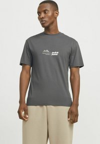Grå bomulds t-shirt med korte ærmer, rund hals og et hvidt logo med bjerge og tekst på venstre brystområde.
