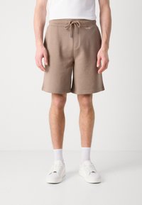 Brązowe bawełniane krótkie spodenki dresowe z regulowanym sznurkiem w talii, bocznymi kieszeniami oraz logo Calvin Klein z przodu. Połącz z białymi butami i skarpetami.