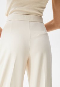 Pantalones de pierna ancha color crema con una textura suave, con una cinturilla plana y un pequeño bolsillo trasero.