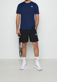 Marinblå atletisk t-shirt med en liten vit logotyp, i kombination med svarta shorts med en sidologotyp, vita strumpor och vita sportskor.