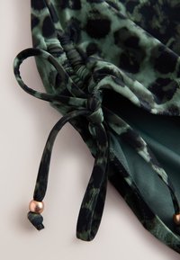 Close-up of green and black leopard print fabric with gathered elastic and tied drawstrings ending in small gold beads.