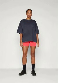 Oversized marineblauwe sweatshirt, roze sportshorts, zwarte sokken en zwarte sneakers. Glad materiaal, losse pasvorm en korte mouwen.