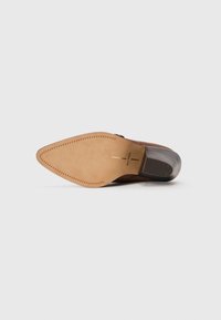 Suela de zapato de cuero marrón con punta afilada, parte inferior de cuero color crema y tacón de goma negra. Presenta un detalle de costura alrededor del borde.