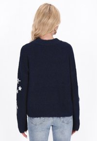 Dunkelblauer gestrickter Pullover mit lockerer Passform, langen Ärmeln und weißer floralem Stickerei am linken Ärmel.