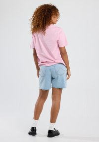 Pink short-sleeve t-shirt paired with light blue denim shorts with frayed hems, worn with white socks and black shoes.