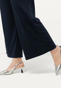 Slingback boty s lesklým stříbrným povrchem a geometrickým podpatkem, spárované s námořnickými kalhotami s širokými nohavicemi, které mají hladkou texturu.