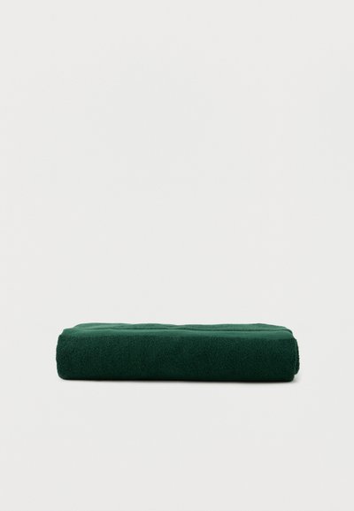 Σκούρο πράσινο διπλωμένο πετσέτα σε απλό λευκό φόντο, που δείχνει μαλακό, υφασμάτινο ύφασμα με υφή και ορθογώνιο σχήμα.