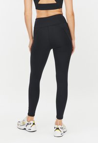 Zwarte sportlegging met een hoge tailleband, naadloos ontwerp en een zachte textuur, gecombineerd met witte en gele sneakers.