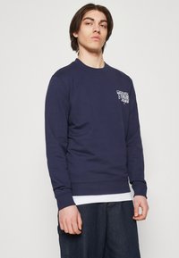 Felpa navy realizzata in misto cotone, con scollo rotondo, polsini a costine e un piccolo logo sulla parte sinistra del petto.