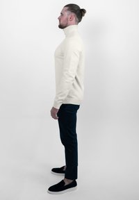 Crème turtleneck trui met een slim fit, geribbelde manchetten, gecombineerd met donkere broeken en zwarte instap schoenen. Soepele textuur, minimalistisch ontwerp.