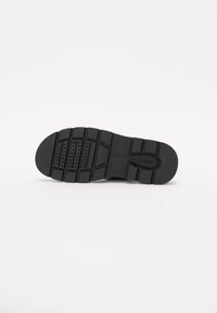 Semelle de chaussure en caoutchouc noir avec des crampons profonds, motifs rectangulaires et points pour l'adhérence, marquée "Geox" sur fond blanc.