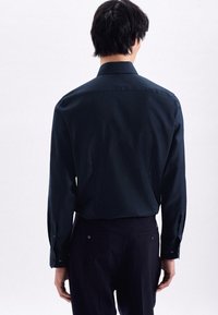 Camicia blu navy con colletto classico, texture liscia e maniche lunghe; presenta un retro sfiancato e polsini con bottoni.