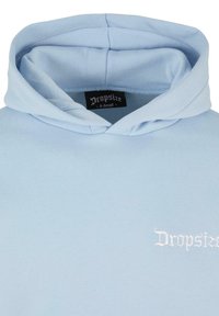 Sweat à capuche bleu clair avec capuche pliée, marque "Dropsize" visible sur une étiquette noire à l'intérieur du col et logo blanc sur la poitrine.