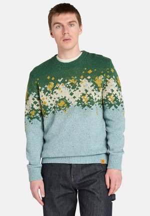 Maglione lavorato a maglia in teal con motivi bianchi e gialli. Presenta un collo a giro, polsini e orlo a costine, e una piccola etichetta con logo sul lato.