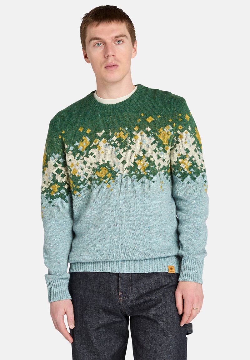 Sweter dziany w kolorze teal z białymi i żółtymi wzorami. Posiada okrągły dekolt, ściągacze przy mankietach i dolnym hemie oraz małą naszywkę z logo z boku.