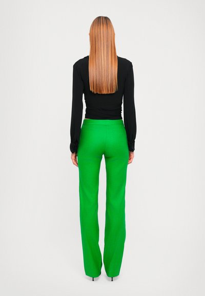Haut noir à manches longues et pantalon vert taille haute, présentant une coupe droite et une texture lisse, vu de dos sur un fond neutre.