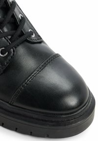 Stivale nero in pelle fino alla caviglia con punta rotonda, superficie testurizzata, cuciture rinforzate e chiusura tradizionale con lacci e occhielli in metallo argentato.
