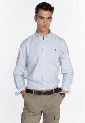Camisa abotonada de color azul claro, hecha de algodón, que presenta un collar clásico y un logotipo bordado en el lado izquierdo del pecho. Diseño ajustado con mangas largas.