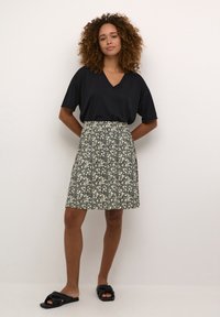 Black v-neck t-shirt, floral-patterned knee-length skirt in dark colors, smooth texture, paired with black sandals. Model stands with hands on hips.