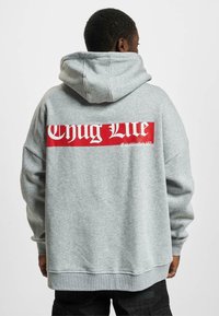 Felpa grigia con una grafica rossa "Chug Life" sul retro. Presenta un cappuccio e una vestibilità ampia, realizzata in tessuto morbido e con texture.