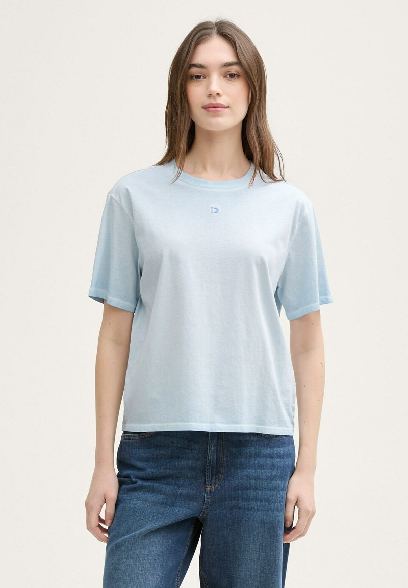Tricou din bumbac de culoare albastru deschis, cu mâneci scurte, croială lejeră, decolteu rotund și detaliu subtil cu logo pe piept. Poartă-l cu blugi de culoare albastru închis.