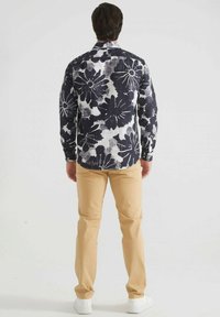 Chemise à manches longues à motif floral bleu foncé et blanc, en tissu léger. Associée à un pantalon beige clair et des baskets blanches.