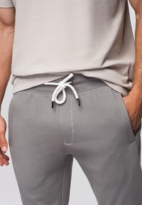 Grijze, lichte joggers met een trekkoord in de taille, voorzien van een witte koord met zwarte uiteinden en twee zijzakken, getoond in een casual setting.