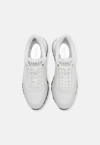 Weiße Athletikschuhe aus Leder mit glatter Oberfläche, ausgestattet mit Schnürsenkeln, einem gepolsterten Kragen und einer schwarzen Gummisohle. Dezente Logo-Details.