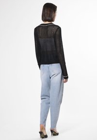 Schwarzer Netzpullover mit langen Ärmeln, gerippten Bündchen und rundem Ausschnitt, kombiniert mit hellblauen hochtaillierten Jeans und schwarzen Absätzen.