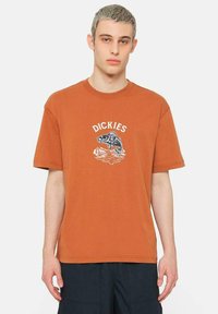 Camiseta de algodón naranja con mangas cortas y cuello redondo. Presenta un gráfico de un pez y la palabra "DICKIES" en blanco encima del diseño.