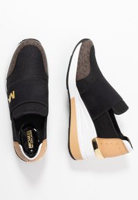 Basketballs noires et marron à enfiler avec un dessus en maille, une bande élastique sur le dessus, une semelle blanche et beige, et un détail en ton doré au niveau du talon, exposées sur fond blanc.