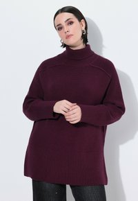 Burgundowy sweter dziany z wysokim kołnierzem, prążkowaną strukturą i długimi rękawami. Posiada luźny krój oraz szwy po bokach na dole.