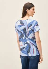 Top de manga corta en azul claro con un patrón floral abstracto en azul oscuro, negro y rojo. Tejido suave con un corte holgado.