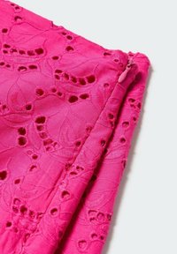 Tissu rose vif avec broderie florale en œillets, plié pour montrer une couture et un tirette de fermeture éclair assorti de couleur rose sur un fond clair.