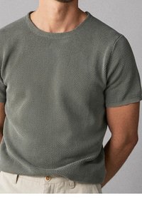T-shirt a maniche corte e collo rotondo in un tessuto verde opaco e testurizzato. Presenta un motivo sottile e una silhouette aderente, con un orlo semplice.