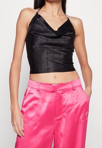 Svart satin crop top med cowl neck och silverfärgade kedjespännen, matchad med klara rosa satinvida byxor med sidfickor och logodetalj.
