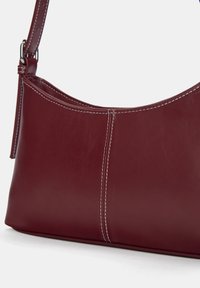 Burgunderfarbene Leder-Schultertasche mit glatter Textur, subtilen Nähdetails und einer geschwungenen Silhouette. Verstellbarer Schulterriemen und minimalistisches Design.
