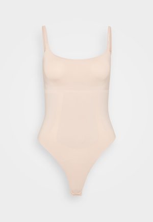 Nude spalvos bodysuit'as su plonais reguliuojamais petnešomis, be siūlių dizainu ir lygiaprekės, tamprios tekstūros. Atgal jis turi stringo tipo kirpimą.