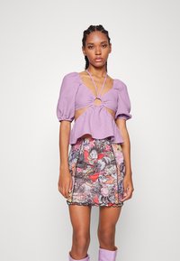 Top lilás de mangas bufantes com detalhe em recorte e acentuação circular, combinado com uma saia mini florido multicolorida com acabamento preto.