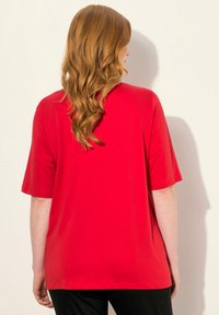 Camiseta roja de manga corta con un corte relajado, hecha de una tela suave. La parte posterior presenta un diseño simple con una textura lisa y un dobladillo curvado.