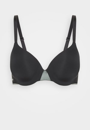 Soutien-gorge noir à armatures avec des coques lisses, des bretelles réglables et un accent triangulaire vert contrastant au centre. Matériau doux sur l'ensemble.