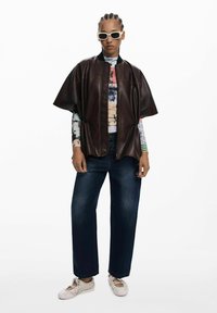 Giacca in pelle marrone, vestibilità ampia, con colletto rotondo e cordoncino. Abbinata a jeans a gamba larga blu scuro e scarpe beige senza lacci.