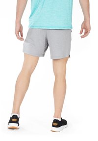 Pantalones cortos deportivos grises de tejido ligero, con un diseño sencillo y aberturas laterales para mayor flexibilidad, combinados con zapatillas negras.